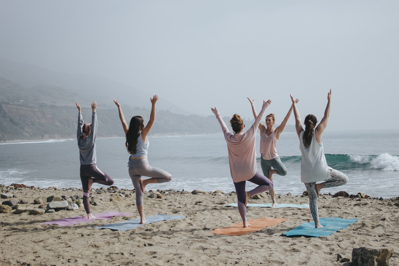 Groupe de femmes pratiquant le yoga sur la plage, bras levés vers le ciel